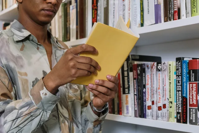 A young adult reading a yellow book in a library setting. Choosing a native format for a reader's information need